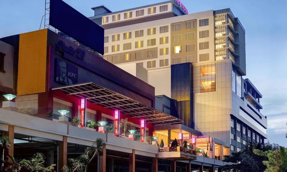 Eksterior hotel modern berwarna putih terang dengan pencahayaan hangat saat malam hari, terlihat bangunan hotel bertingkat dengan teras dan jendela besar